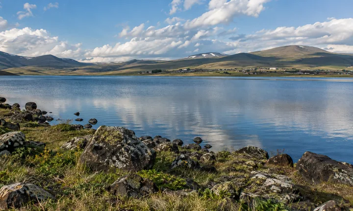 A blue highland lake bordered by grass and dark volcanic stones on Georgia's plateau A blue highland lake bordered by grass and dark volcanic stones on Georgia's plateau