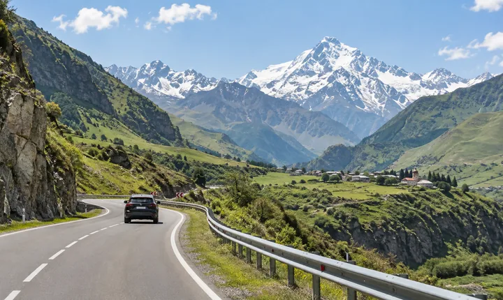 A dark SUV follows a paved winding road through Georgia's green Caucasus foothills A dark SUV follows a paved winding road through Georgia's green Caucasus foothills