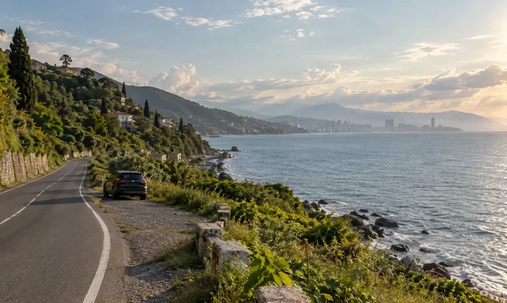 A parked SUV beside a coastal road with Georgia's Black Sea and green foothills beyond A parked SUV beside a coastal road with Georgia's Black Sea and green foothills beyond