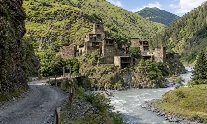 Mountain road entering Shatili valley beside a river and medieval stone tower houses in Khevsureti Mountain road entering Shatili valley beside a river and medieval stone tower houses in Khevsureti