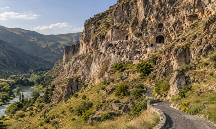 Vardzia cave monastery cut into a tan cliff above the green Mtkvari valley and its access road Vardzia cave monastery cut into a tan cliff above the green Mtkvari valley and its access road