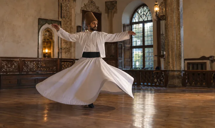 A whirling dervish in a white robe inside a modest historic hall